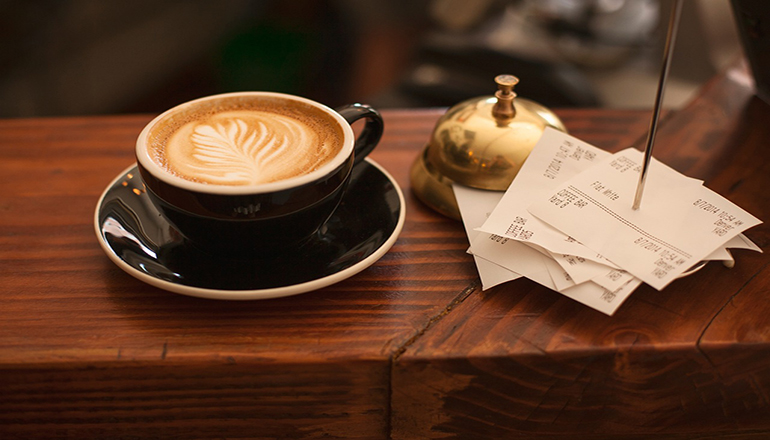 En bardisk med en kopp kaffe och en hög med kvitton.