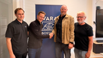 Fyra män framför en rollup med Vara Bostäders logotyp. Två skakar hand.